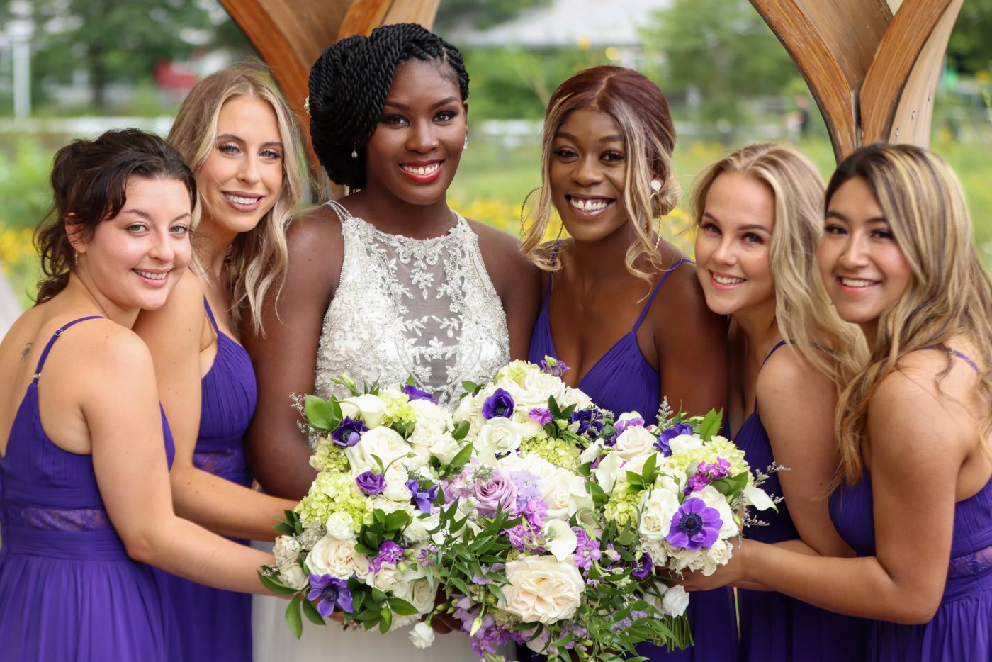 Bride with her bridesmaids in purple dresses, smiling around her bouquet