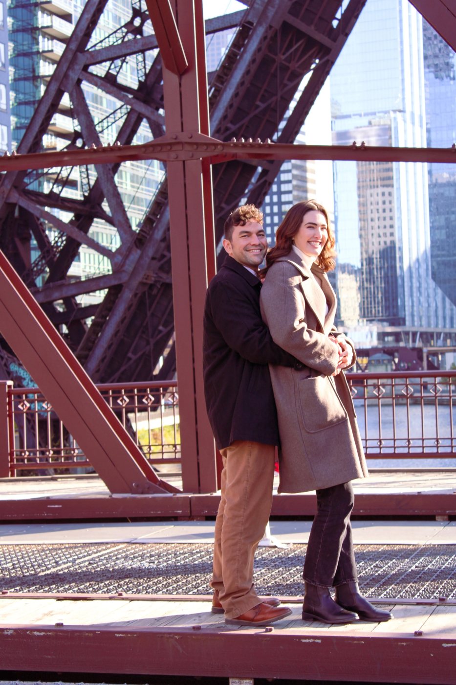 Couple embracing on a red steel bridge with the Chicago skyline behind them